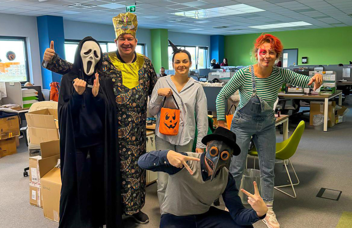 Pracownicy Lynka w strojach na Halloween pozują w biurze wśr&oacute;d dekoracji.